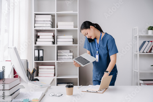 Busy Healthcare Professional: A focused healthcare worker juggles multiple tasks, talking on the phone, holding a laptop, and reviewing a chart in an organized office setting.