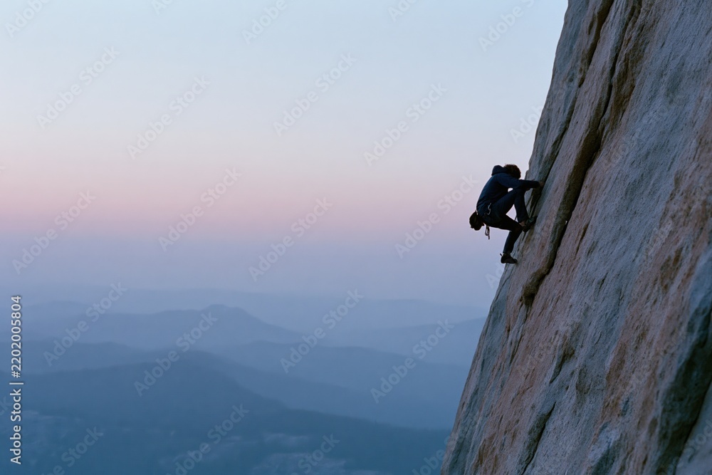 Obraz premium The Climber Mastering a Steep Cliff at Dawn Across Expansive Mountain Range
