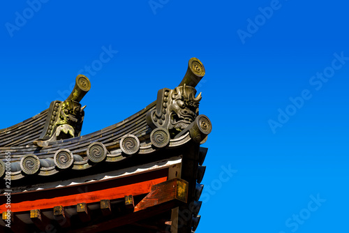 A traditional Japanese roof corner adorned with onigawara against a blue sky. The demon-faced roof tile is traditionally used in Japanese architecture to protect buildings and scare away evil spirits.