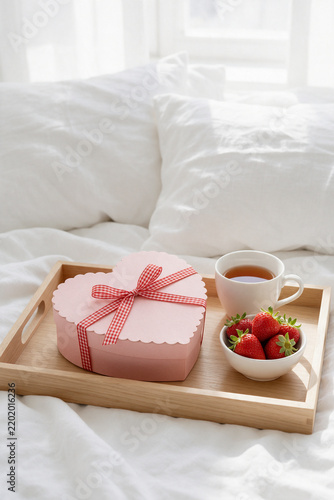 Pink heart gift box on wooden breakfast tray with tea and strawberries