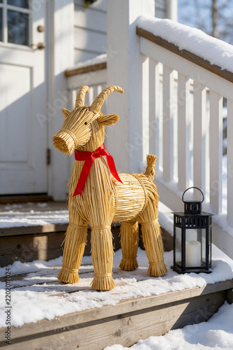 Straw Yule goat with red ribbon and lantern on snowy wooden porch