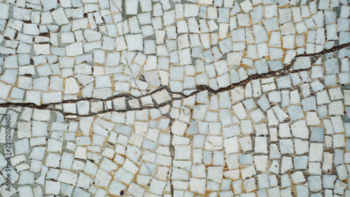 Old cracked mosaic floor texture with white tiles and damage