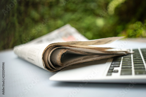 Newspaper on top of computer laptop outdoor.
