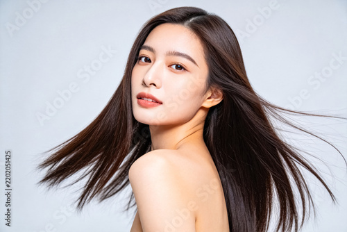 Young East Asian woman with long straight dark hair posing against light gray background