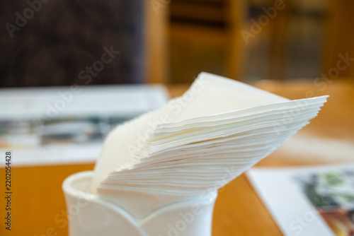 Stack of white paper napkins neatly arranged in a ceramic holder on a wooden dining table in a hotel restaurant.