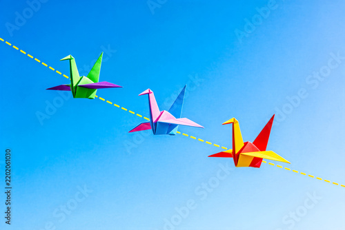 Three Colorful Origami Cranes Flying Against Clear Blue Sky