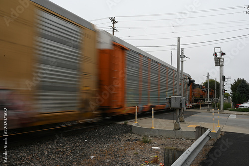 Freight train crossing roadway in city, train cars blurred to illustrate motion.