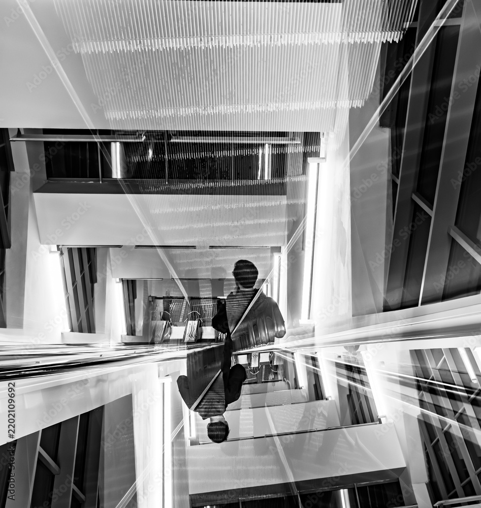Fototapeta premium Abstract black and white double exposure of a man on escalator in modern building architecture, conceptual symmetrical urban design