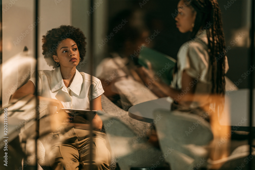 Obraz premium Two businesswomen having conversation through glass office partition at golden hour