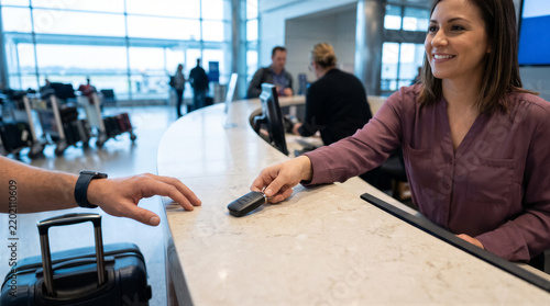 Friendly car rental agent handing over keys to a customer at a busy airport service counter