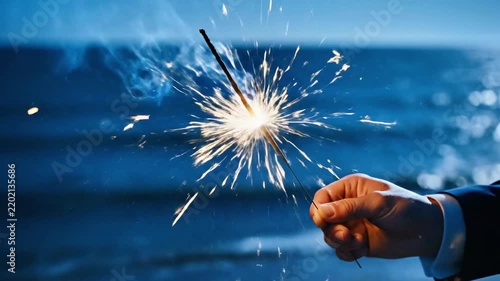 Hand Holding a Glowing Sparkler Celebrating on a Sea Beach at Nighttime zamIR