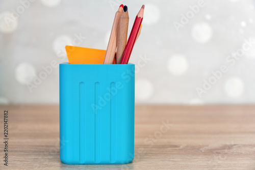 Blue 3D-printed pencil holder with stationery on a wooden desk. Minimalist workspace with bokeh background, ideal for office or education themes
