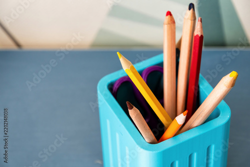 Vibrant colored pencils and scissors in a blue desk organizer. Minimalist school supplies for education, art, and home office. Includes copy space