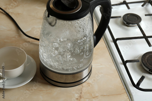 A transparent electric kettle with boiled water on the kitchen table.