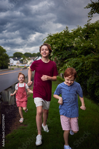 Happy children running together in summer rain under dramatic stormy sky