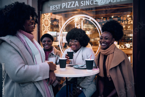 four happy female friends laughing, having fun, socializing at outdoor cafe, dressed for autumn or winter weather.