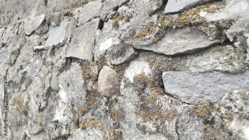 a close-up, angled shot of a rough, irregular stone wall. It appears to be an old, weathered structure, possibly a foundation, fence, or historical building.