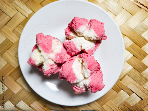 Obraz na plátně Top view of pink and white bolu kukus mekar or Indonesian traditional blooming steamed sponge cupcake served on a white plate over woven bamboo mat background, soft texture and sweet snack