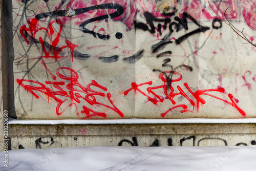 Bright red graffiti tags painted on a weathered concrete wall background, contrasting with pristine white snow during a crisp winter day