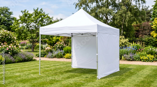 A pristine white pop-up canopy tent with a side wall stands on a vibrant green lawn in a beautifully landscaped garden.