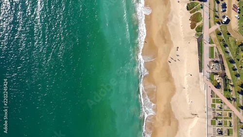 Aerial drone footage moving along a sandy beach in Viña del Mar as turquoise Pacific waves reach the shore beside a coastal promenade.