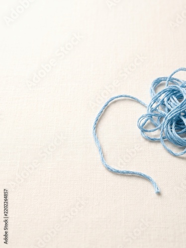 Loose blue thread rests on white fabric. A tangled coil sits at the right edge with a long strand crossing the textured surface and copy space. Craft, sewing, and handmade design concept.