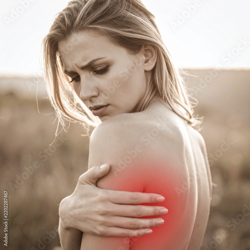 Blonde woman with smooth skin holding her aching shoulder highlighted by vibrant red glow indicating severe pain.