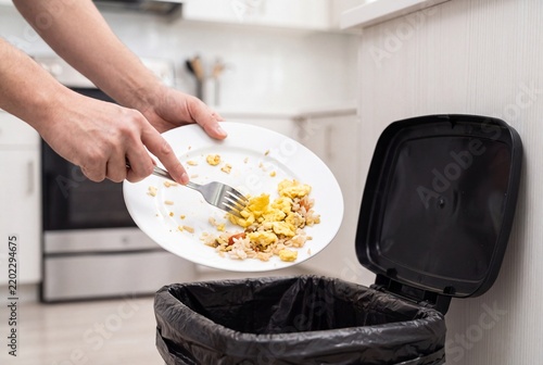 Person Scraping Food Leftovers from Plate into Trash Can in Kitchen