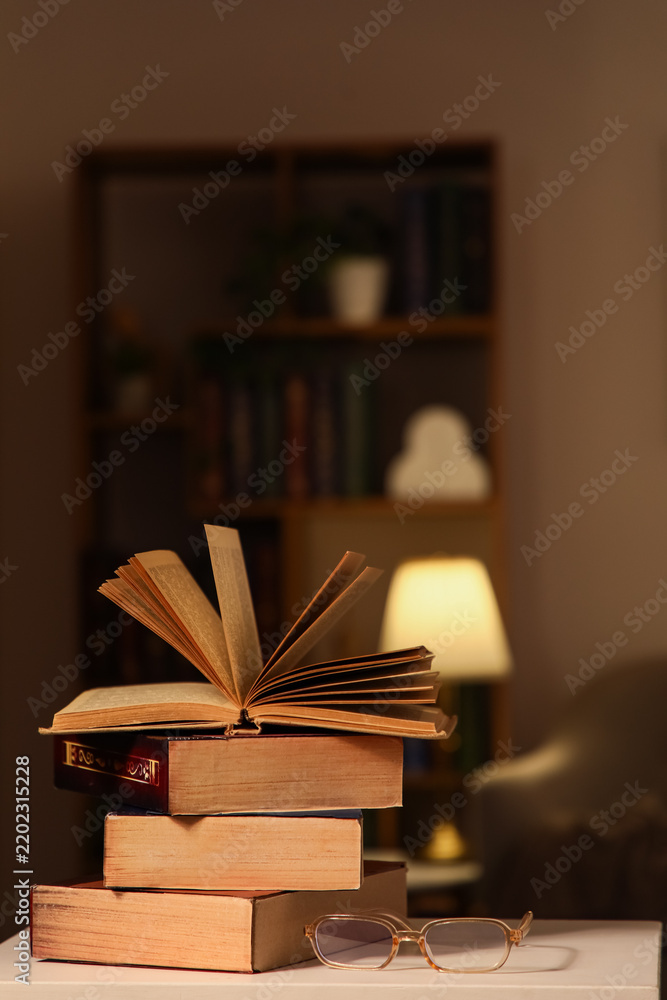 Obraz premium Education and lifelong learning, open book on a stack of vintage books with reading glasses in a cozy library room with warm lamp light at night