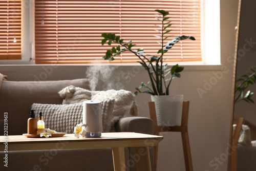Aroma diffuser with essential oils and plumeria flowers on table in living ro...