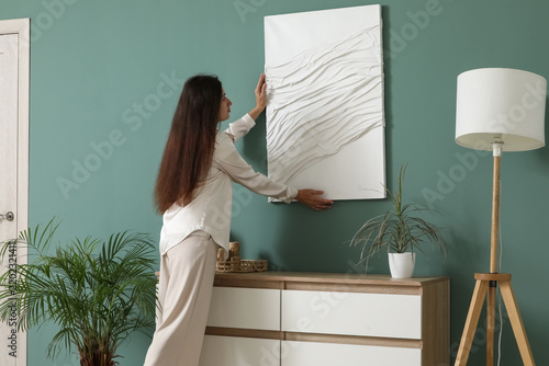 Young woman hanging picture on green wall at home, closeup