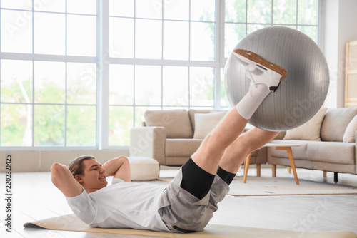 Sporty young man training with fitball at home