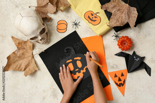 Child with supplies making Halloween decorations on grunge beige background