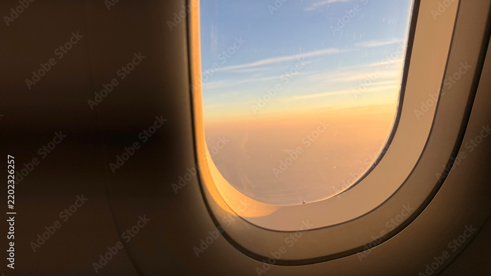 Obraz premium Scenic minimalist view of a golden sunset sky through an airplane window inside the cabin, commercial aviation flight and peaceful travel wanderlust concept