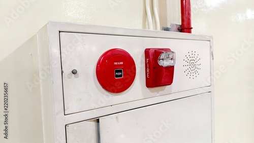 a close-up, angled view of a white, wall-mounted fire protection cabinet set against a light beige wall. The top section of the metal cabinet features integrated emergency equipment