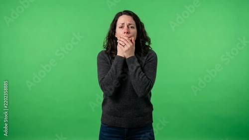 Worried young woman covering her mouth with both hands against a bright green studio background, expressing shock or surprise