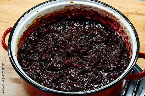 Cooking homemade plum jam in red enamel pot close up