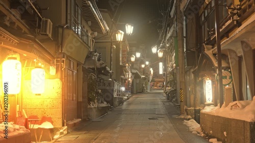 提灯の温かい明かりが灯る雪の温泉街の夜の石畳スローモーション