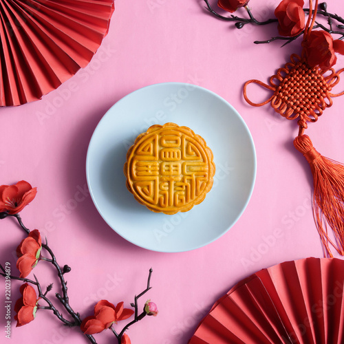 Chinese mooncake on blue plate with festive red fans and knot decor on pink background
