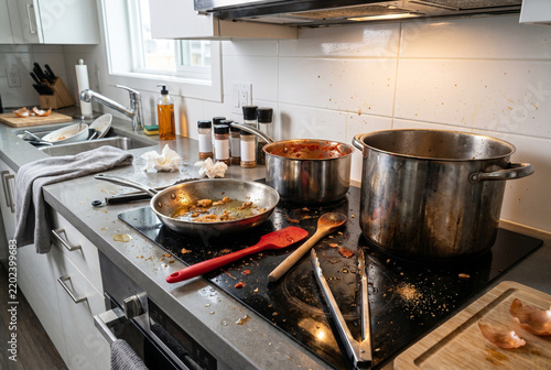 Messy kitchen stovetop with dirty pots and spilled food debris  