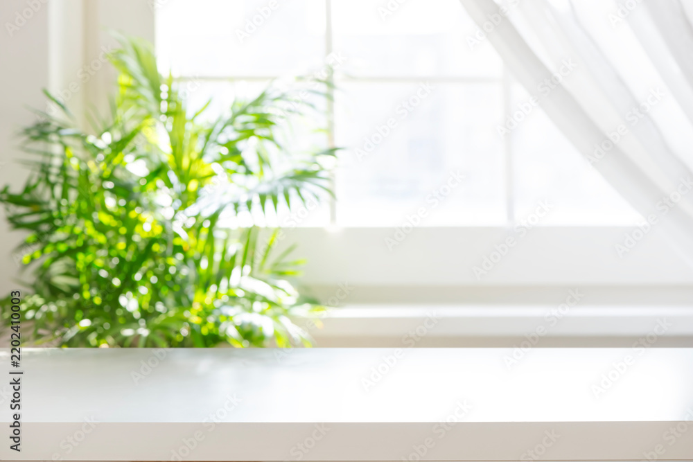 Fototapeta premium White table top with blurred green plant near a sunny window background