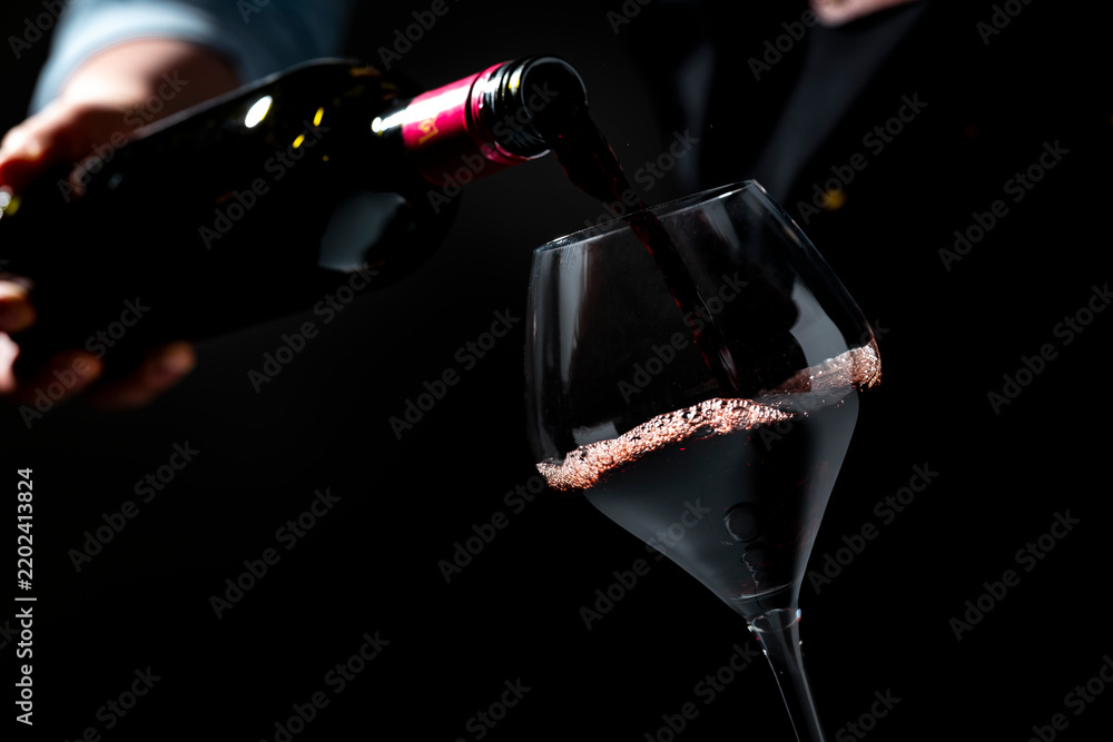 Obraz premium Authentic Malbec red wine splashing in glass — gourmet lifestyle concept. Restaurant sommelier with dark bottle pouring alcoholic beverage. Hospitality industry, fine dining celebration.
