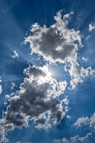 Teilweise verdeckte Sonne hinter vom Wind zerzausten Schönwetterwolken mit Lichtstrahlen