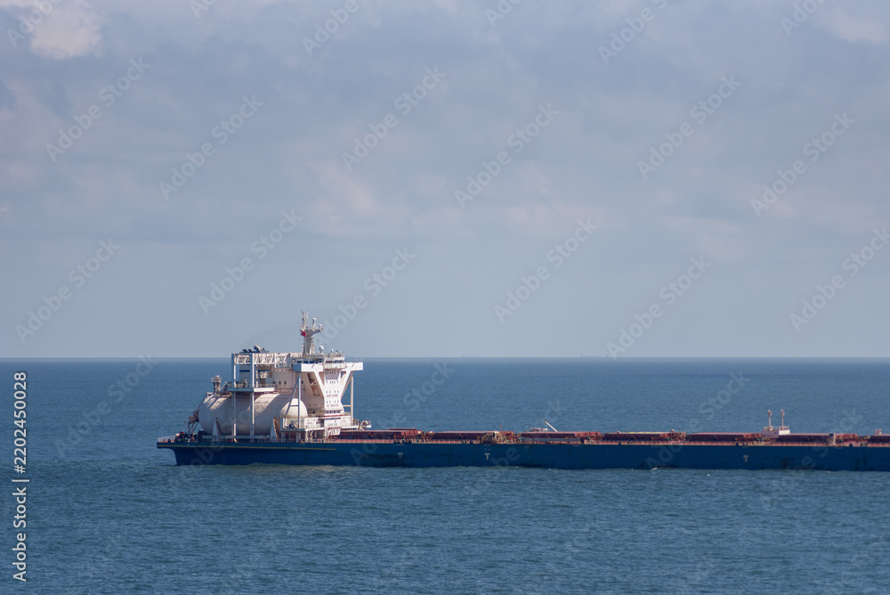 Fototapeta premium Large LNG-powered bulk carrier sailing slowly across calm blue waters, with the distinctive LNG fuel tank visible near the superstructure.