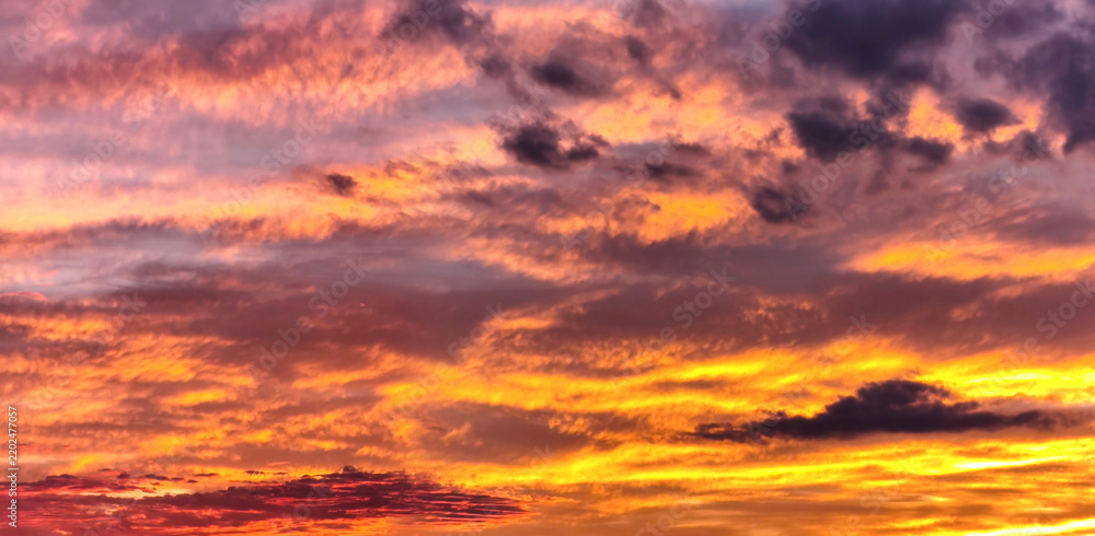 Obraz premium Vivid dramatic sunset sky with golden orange, pink and purple clouds, colorful evening cloudscape at dusk, beautiful natural background with warm glowing light and deep blue tones