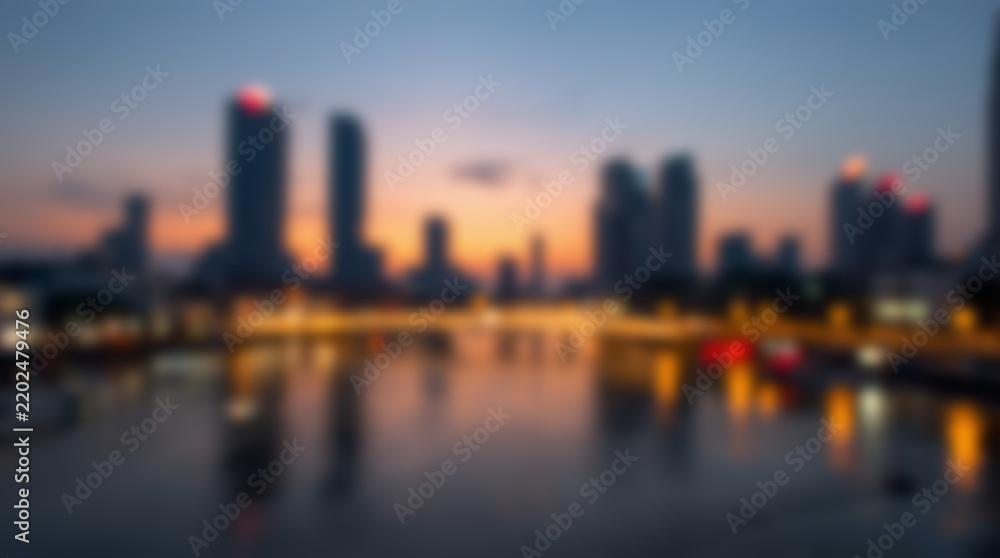Fototapeta premium Blurred city skyline at dusk with reflections in water.