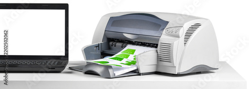 Printer and laptop on a white table with printout being processed