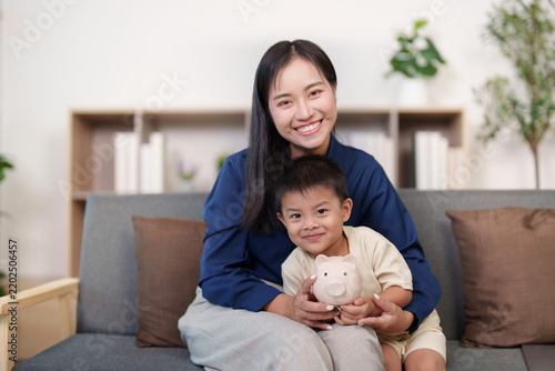 Happy Asian mother and son holding piggy bank for family financial wellness and savings