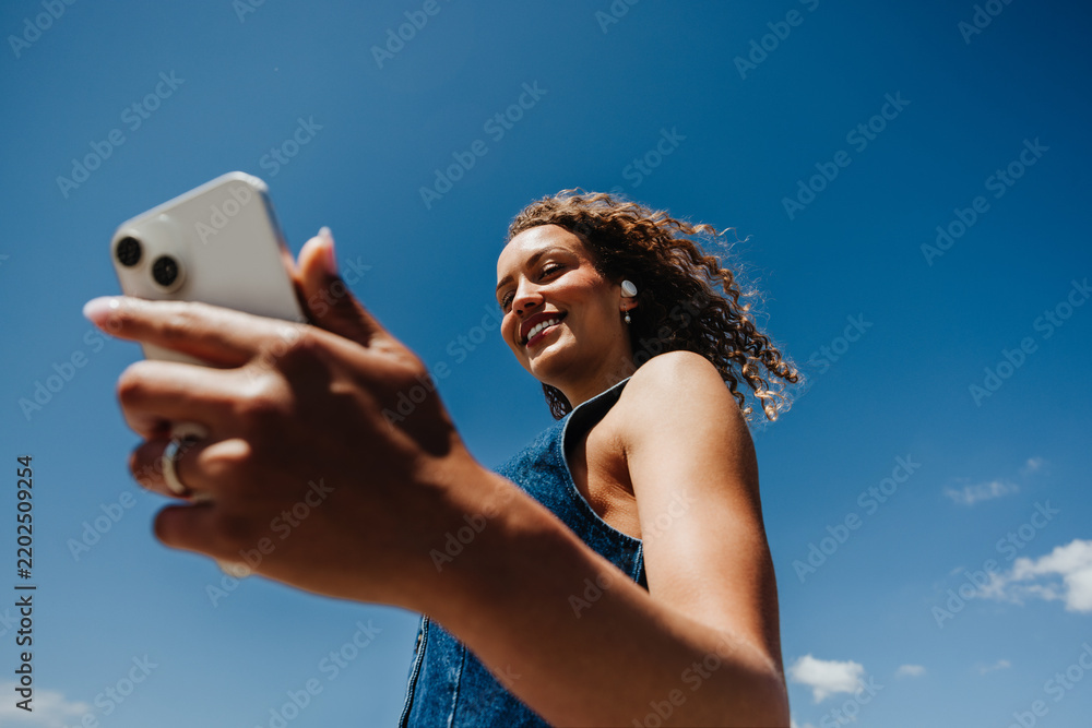 Obraz premium Woman checks smartphone while listening to music outdoors under blue sky