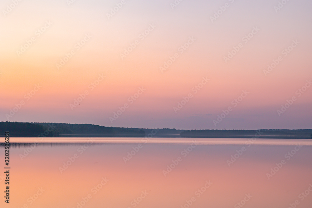 Obraz premium Peaceful sunset reflections over a calm Finnish lake during twilight in Finland. Soft pastel shades of pink, orange, and purple color the gradient sky and smooth water